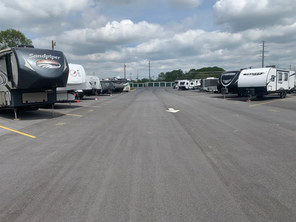 Ground-level view down a wide paved lane between rows of stored RVs and travel trailers